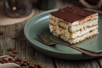 A piece of Tiramisu cake, traditional Italian dessert, served in moody, rustic scene. Wooden background and green plate. 