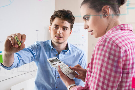 Young Man and Young Woman Working in an Office, Looking Through Glass Board, Germany