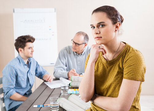 Portrait of Young Businesswoman Leaning on Hand with Colleagues Meeting in the Background