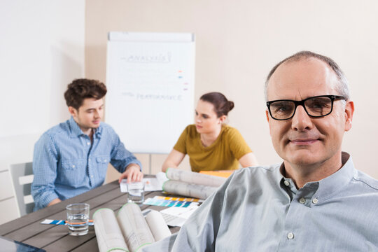 Portrait of Mature Businessman wearing Eyeglasses with Colleagues Meeting in the Background
