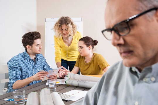 Close-up of Mature Businessman with Young Colleagues Meeting in Background