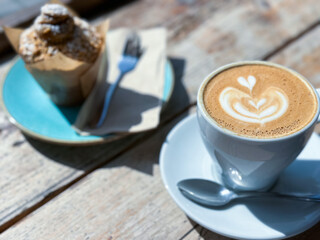 Cup of fresh flat white or latte coffee with muffin on wooden background. French style breakfast in a cafe. Latte art coffee with freshly baked muffin on a wooden table. pov