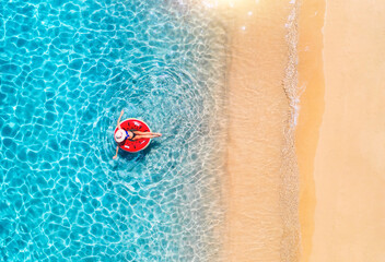 Aerial view of a woman in hat swimming with red swim ring in blue sea at sunset in summer. Tropical...