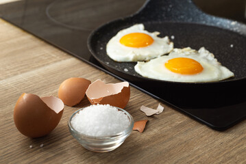 fried eggs with spatula in a frying pan, salt and eggshell on the table