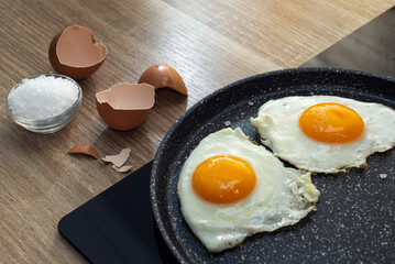 fried eggs in a frying pan, salt and eggshell on the table