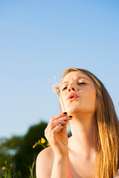 Young woman blowing seeds from dandelion, Germany