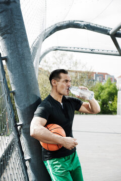 Mature man standing on outdoor basketball court drinking bottle of water, Germany