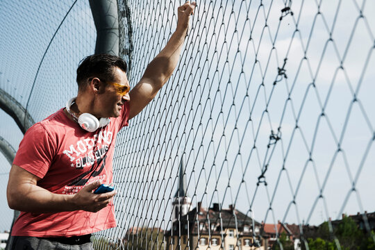 Mature man standing on outdoor basketball court holding MP3 player, Germany