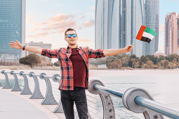 A freelance worker or student embraces the UAE flag, symbolizing his commitment to the nation's values and ideals near Abu Dhabi skyscrapers