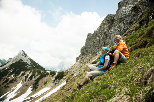 Mature couple sitting on grass, hiking in mountains, Tannheim Valley, Austria