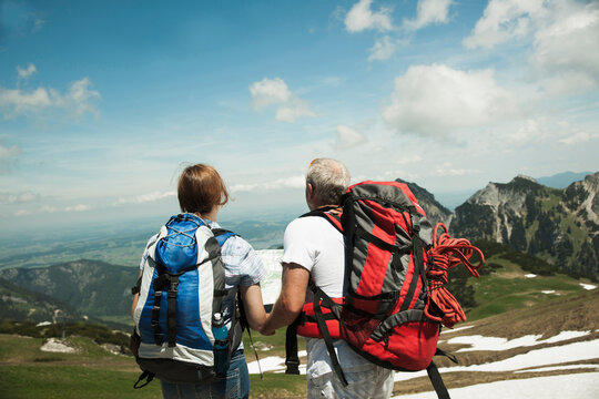 Backview of mature couple looking at map, hiking in mountains, Tannheim Valley, Austria