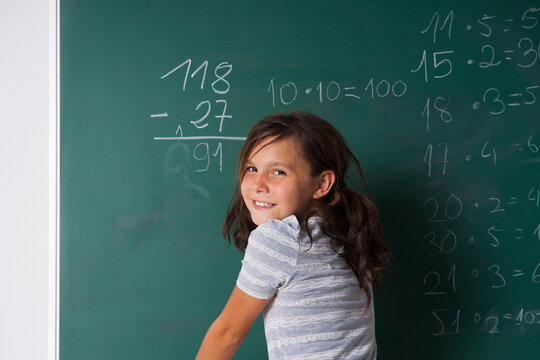 Girl standing in classroom in front of blackboard dong mathematical questions, Germany