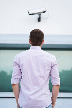 Backview of young man standing outdoors, looking at security camera, Germany