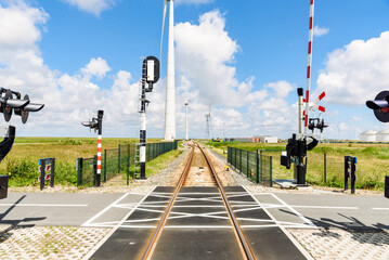 Level crossing along a railway to a commercial port on a sunny summer day. Wind turbines line the tracks.