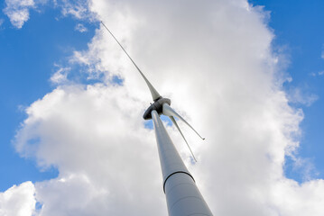 View from below of a wind turbine against blue sky with clouds in summer