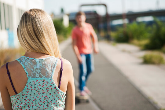 Backview of teenage girl in foreground and teenage boy on skateboard in background, Germany