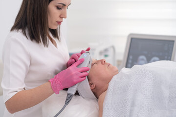 Professional equipment is used to perform a SMAS ultrasound face lifting massage on a relaxed female client at a beauty center. 