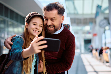 Happy father and daughter taking selfie at train station.