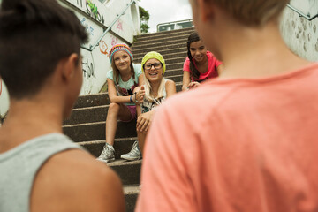 Backview of two boys talking to girls sitting on stairs outdoors, Germany