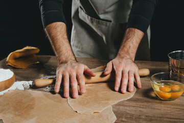 Unrecognizable man rolling out the dough with a rolling pin on wooden background