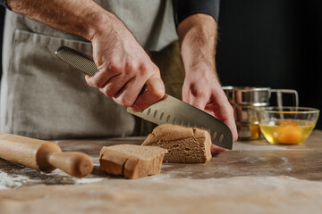 Unrecognizable man cutting the dough with a knife on a wooden background