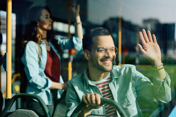 Happy man waves to someone through window while riding in bus.