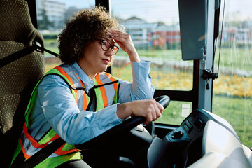 Female bus driver having headache while sitting behind steering wheel.