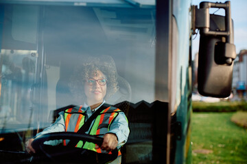 Happy female bus driver looks at side view mirror while parking in reverse at station.