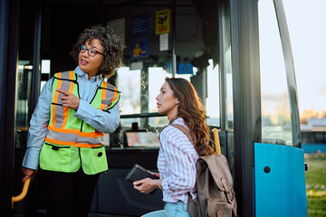 Bus driver assists young woman with a direction at station.