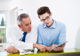 Businessman and apprentice looking at talet computer in office, Germany