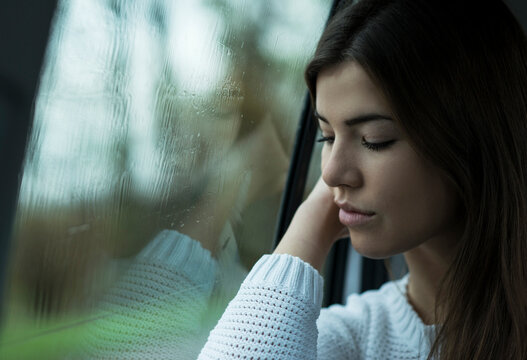 Portrait of young woman sitting inside car next to window, looking downwards and day dreaming on overcast day, Germany