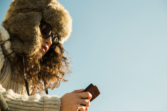 Close-up of teenage girl outdoors, wearing trapper hat and sunglasses, looking down at smart phone, Germany