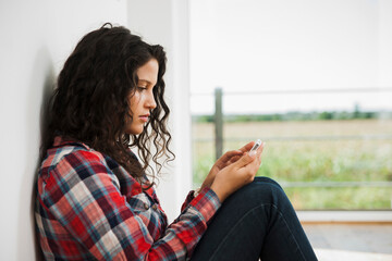 Close-up of teenage girl sitting next to window and using cell phone, Germany