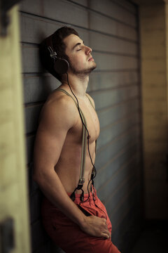 Portrait of young man leaning against wall, wearing headphones and listening to music, Germany