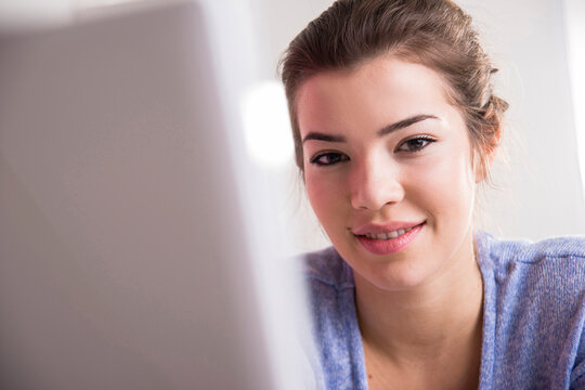 Close-up of young woman working in office on desktop PC, looking at camera and smiling, Germany