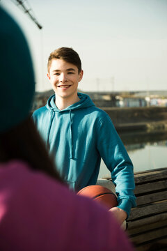 Teeange boy holding basketball outdoors, smiling and looking at teenage girl, industrail area, Mannheim, Germany