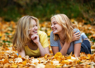 Portrait of two teenage girls laying in the leaves and having fun in a city park on a warm fall afternoon; St. Albert, Alberta, Canada.