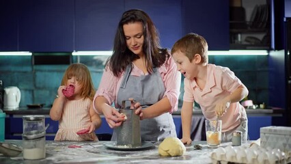 Mother, son and daughter are cooking together in the kitchen. Children help their parents at home. Kids having fun, woman rubs cheese on pizza. Happy together lifestyle. High quality 4k footage