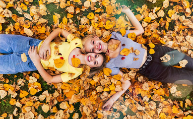 Portrait of two teenage girls laying on the ground in the fallen leaves and looking up at the camera on a warm fall day; St. Albert, Alberta, Canada.