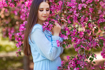Naklejka premium A pretty girl , long hair , stands near a pink blooming apple tree