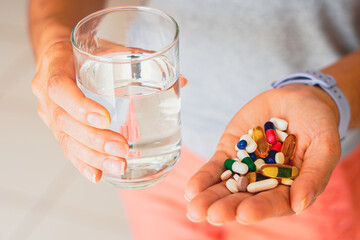 A person holding several medicine pills and a glass of water.