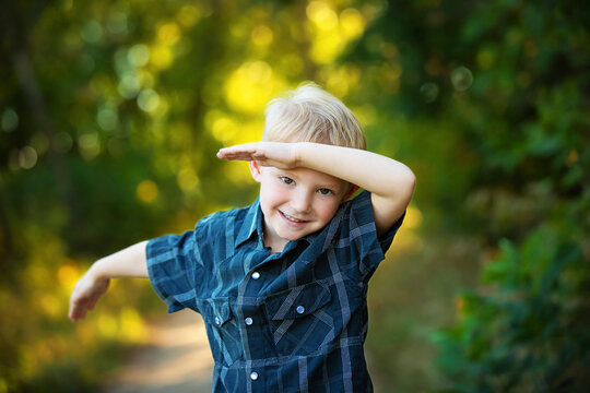 Close-up portrait of a cute young boy with blond hair doing a dance gesture called 'the dab' with a big smile for the camera; Edmonton, Alberta, Canada