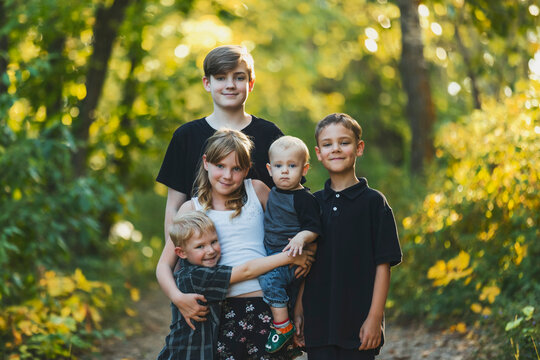 Outdoor portrait of five young siblings standing on a trail in a woodland; Edmonton, Alberta, Canada