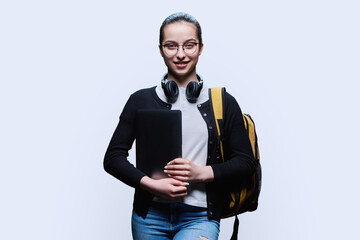 Teenage girl student with backpack holding laptop on white studio background
