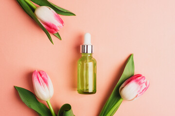 Green serum bottle and tulip flowers on coral pink background. Top view, flat lay, mockup