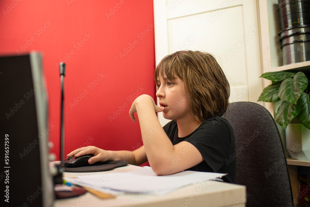 Wall mural the child is sitting at the table, in front of the computer, studying the material of the online les