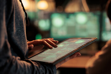 Hacker using spyware on digital tablet for illegal access on network, stealing passwords and cracking firewall encryption at night. Internet criminals hacking financial data, breaking into server.