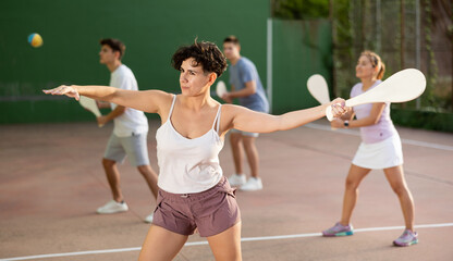 Portrait of sporty young girl playing paleta fronton on outdoor court, ready to hit ball. Healthy and active lifestyle concept