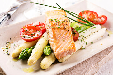 Traditional German green and white asparagus with salmon and tomatoes served as close-up on a design plate