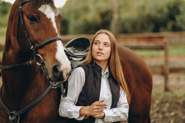 A young female equestrian stands near her horse and prepares for a competition.